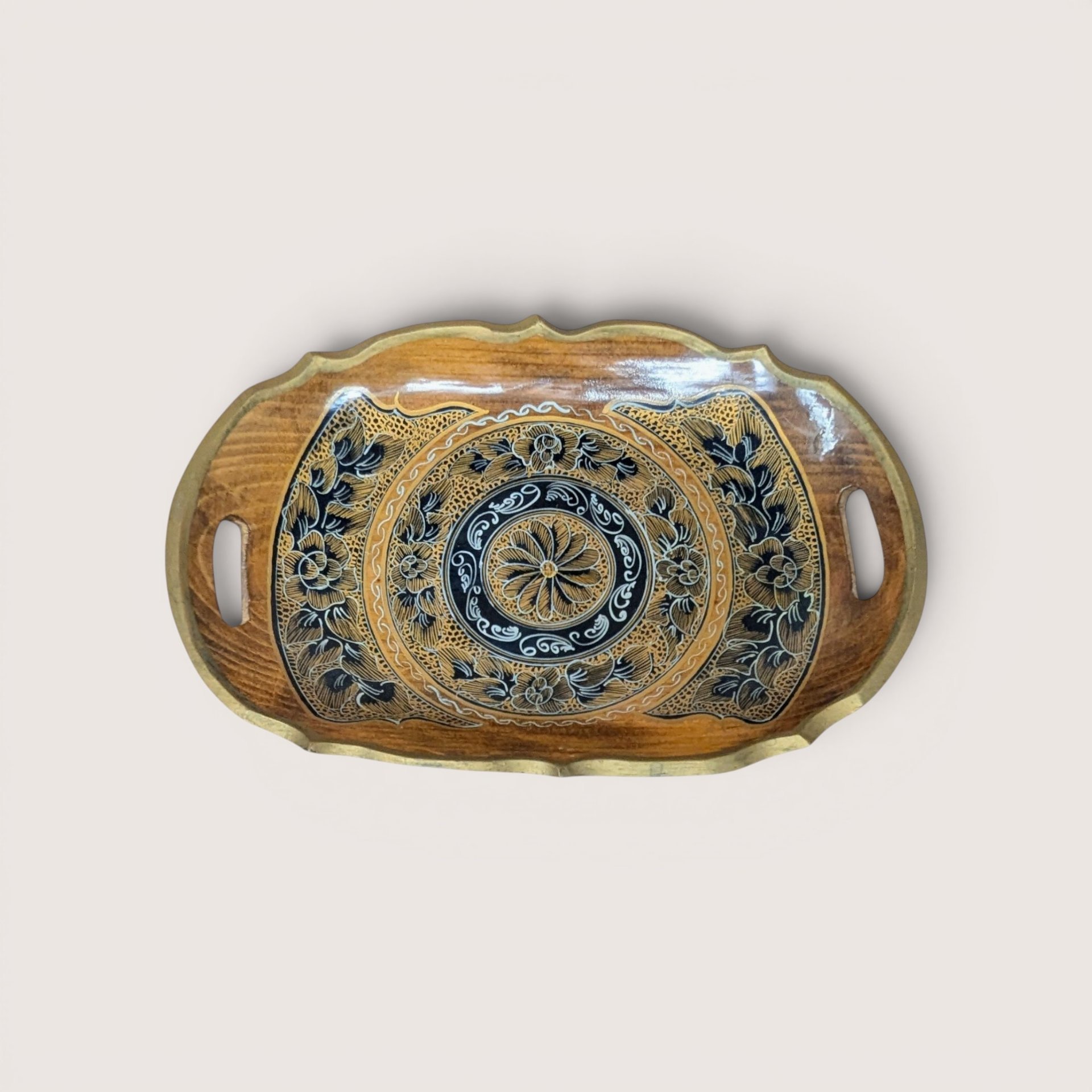 An oval wooden serving tray with intricate black gold and white floral hand painted details on a plain background