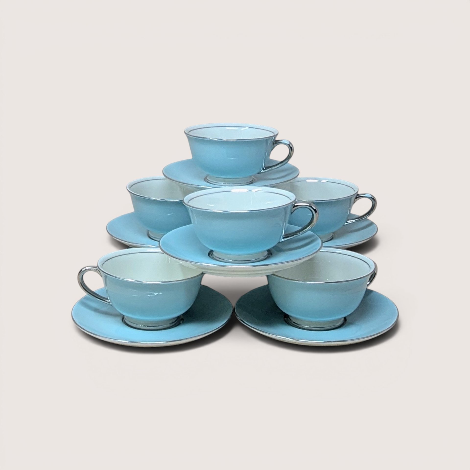 A pyramid stack of six vintage Nancy Prentiss light blue fine china tea cups with matching saucers and silver trim.