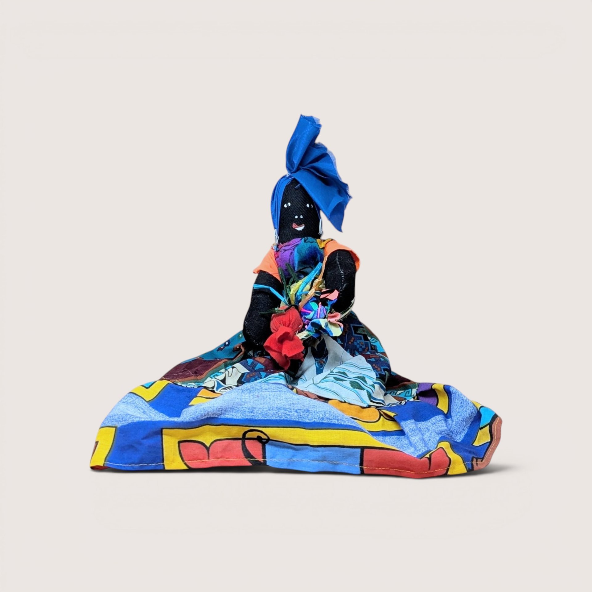 A vintage handmade Black cloth folk art doll wearing a vibrant, colorful abstract dress and a matching blue headwrap.