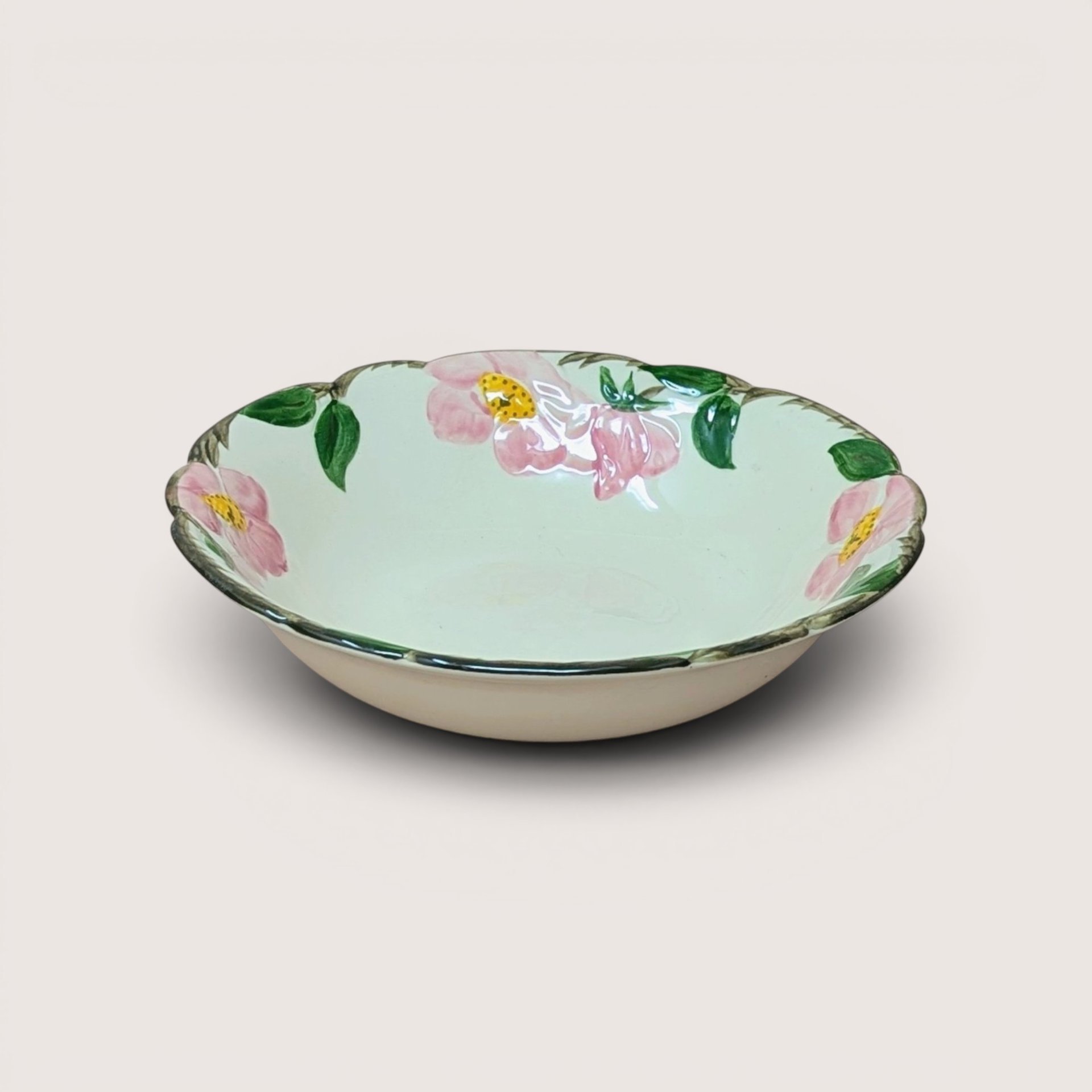 A vintage hand painted ceramic bowl featuring pink roses and green leaves on a cream background with a sculpted edge.
