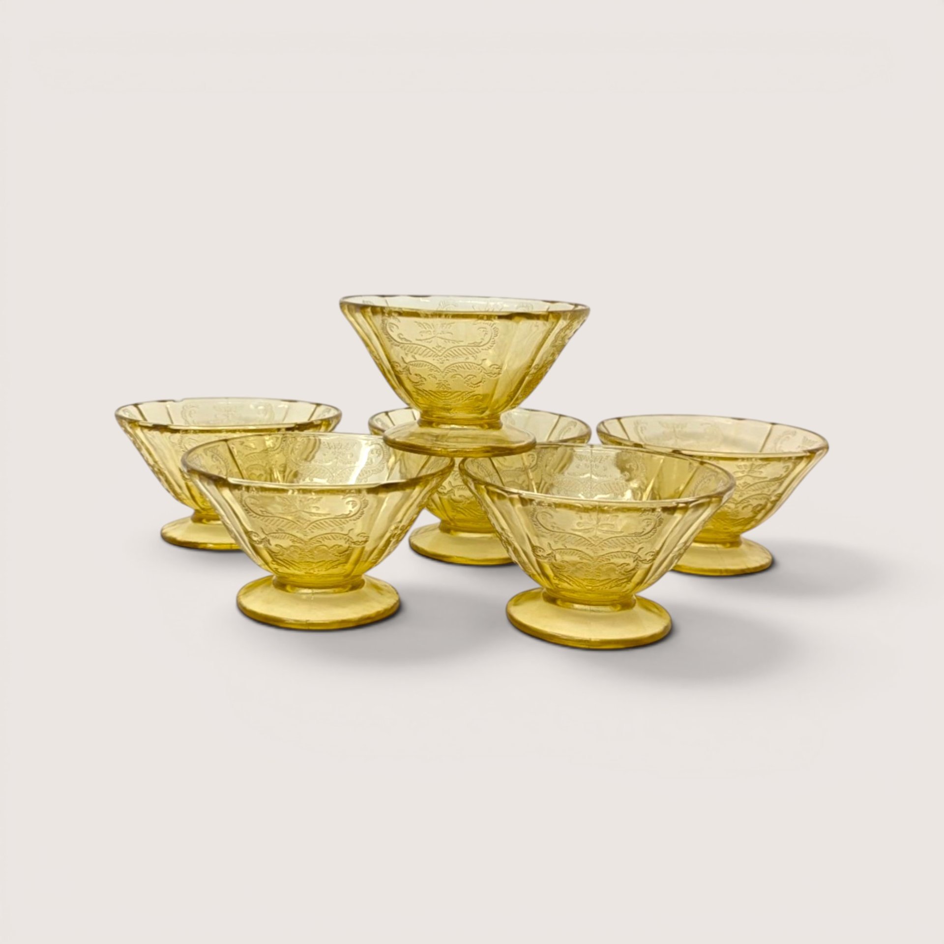 A set of six vintage amber depression glass sherbet cups stacked in a small pyramid on a plain background