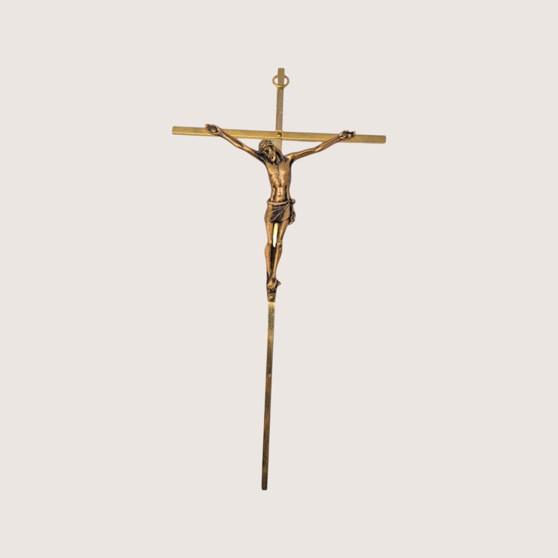 A slim vintage brass colored crucifix wall hanging featuring a detailed bronze tone corpus on a light cream background