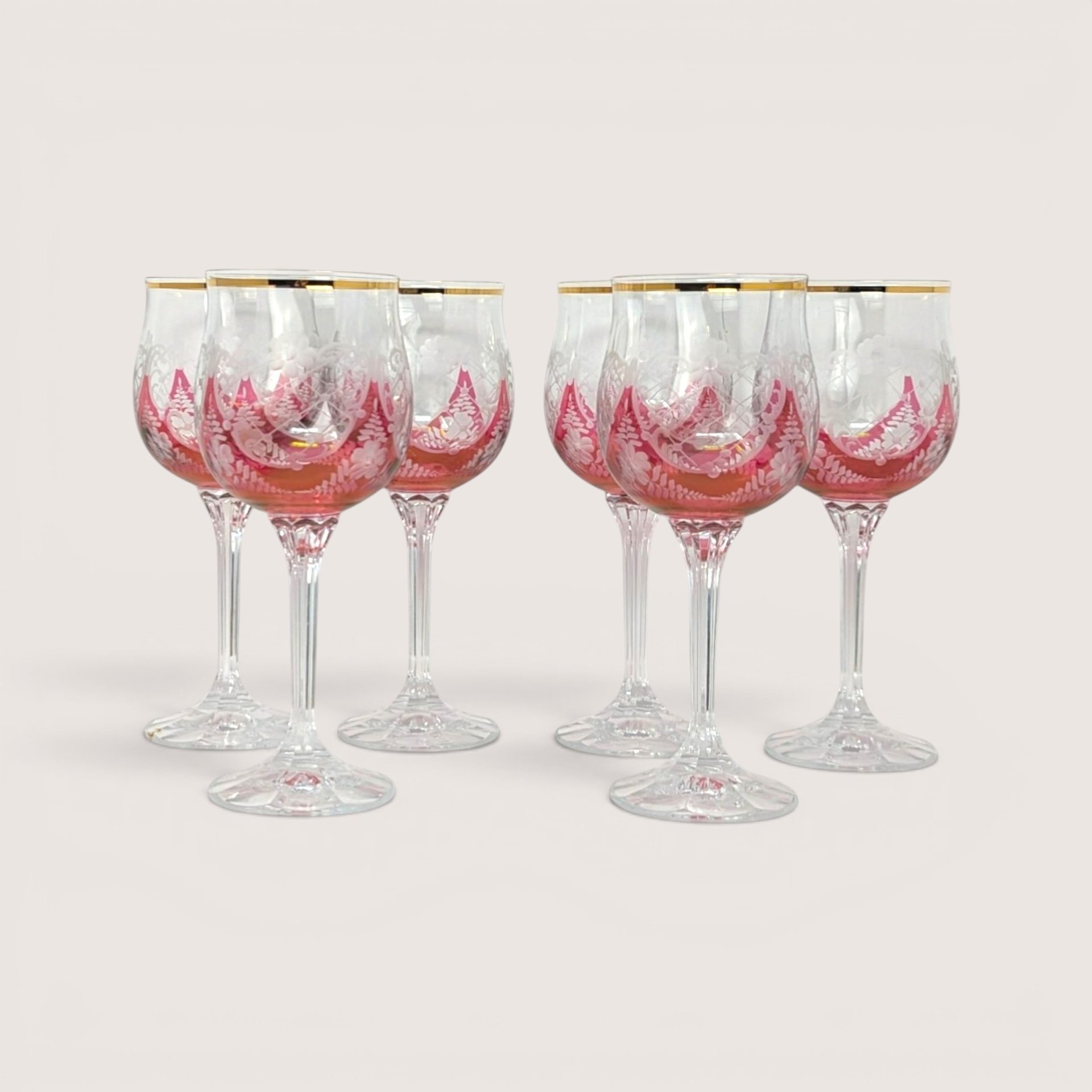 Set of six vintage cranberry red wine glasses with gold rims and white enamel floral details on a book.