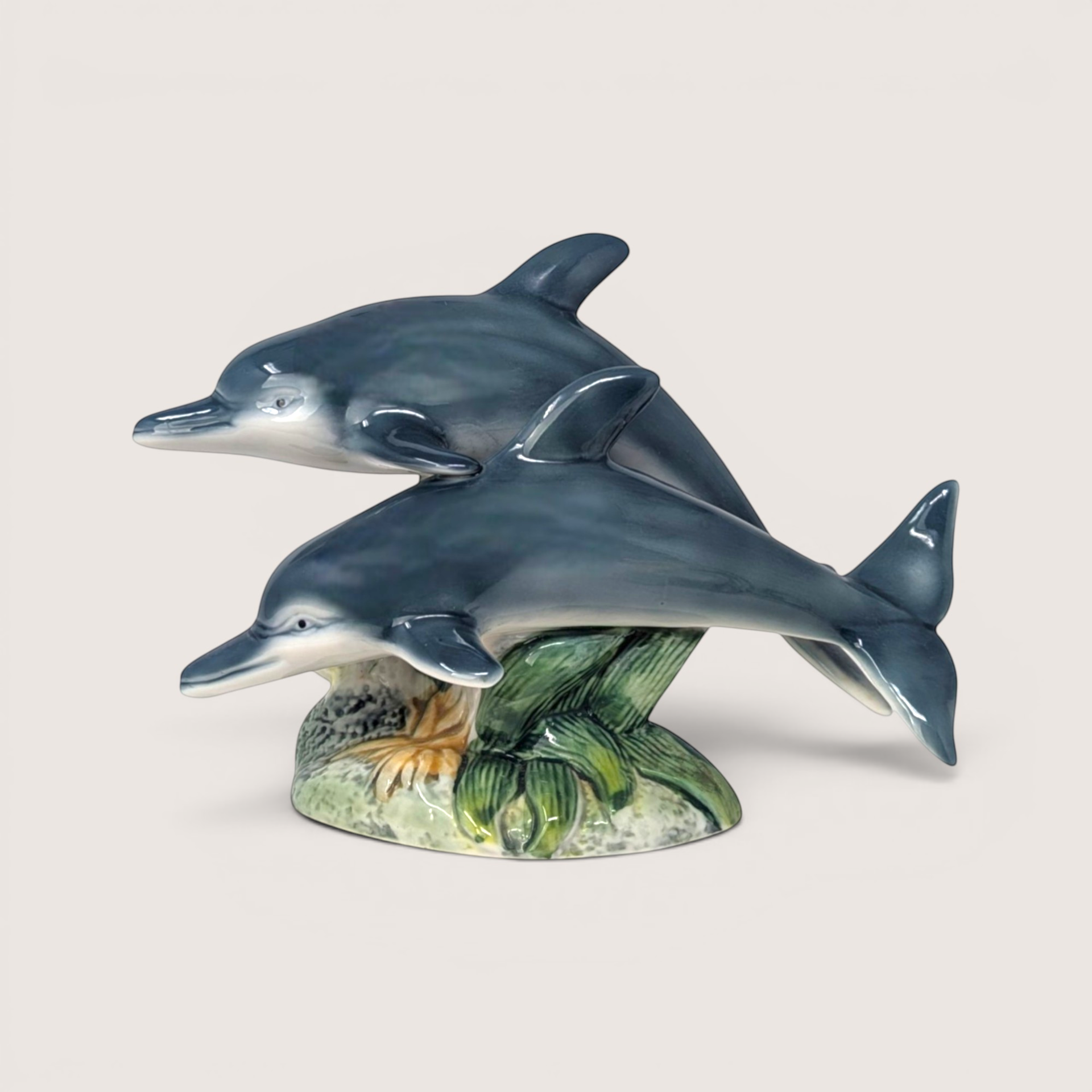 Vintage high-gloss ceramic figurine of two blue-gray dolphins jumping over green seaweed.