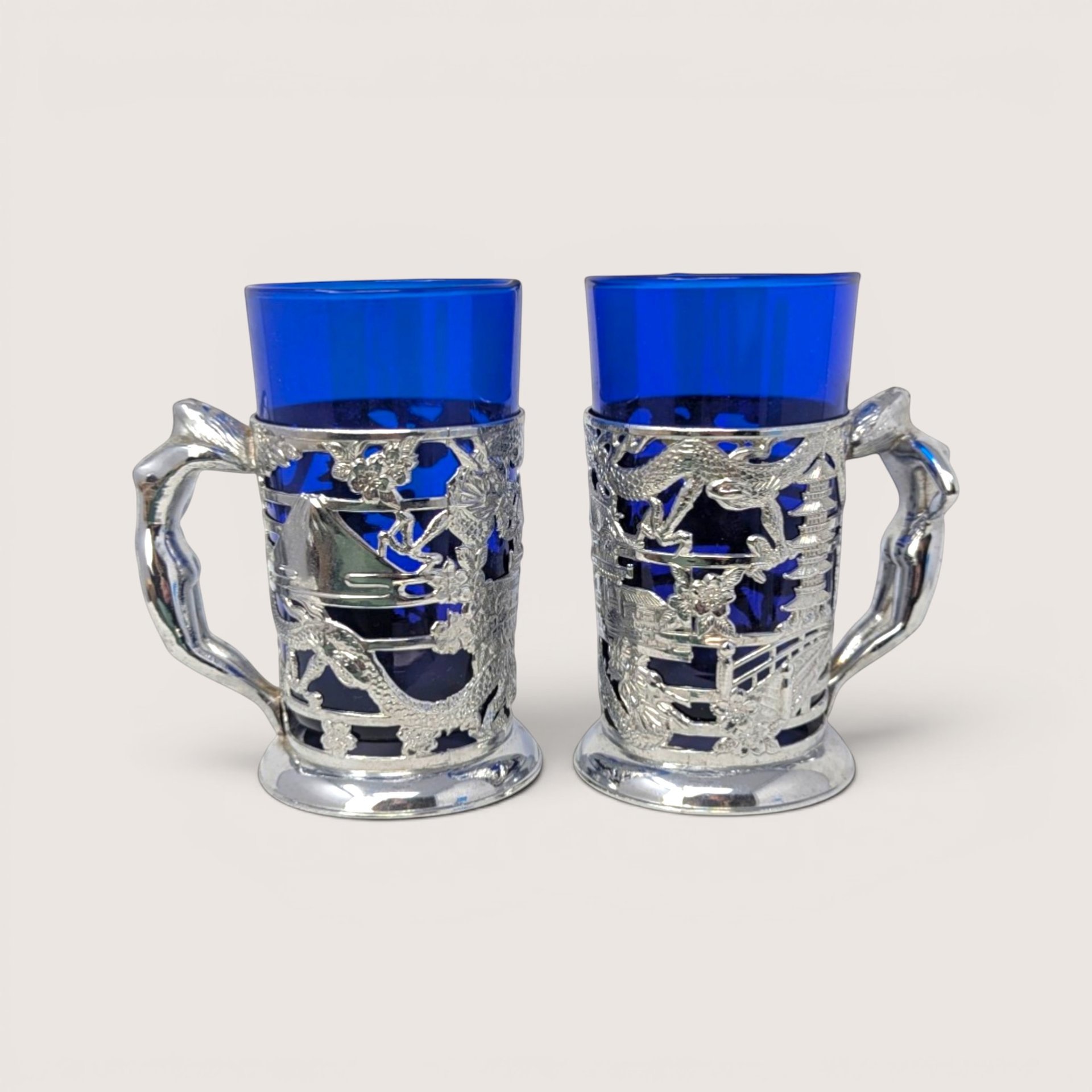 Pair of vintage Japanese silver-plated tankards with cobalt blue glass liners and detailed figural handles.