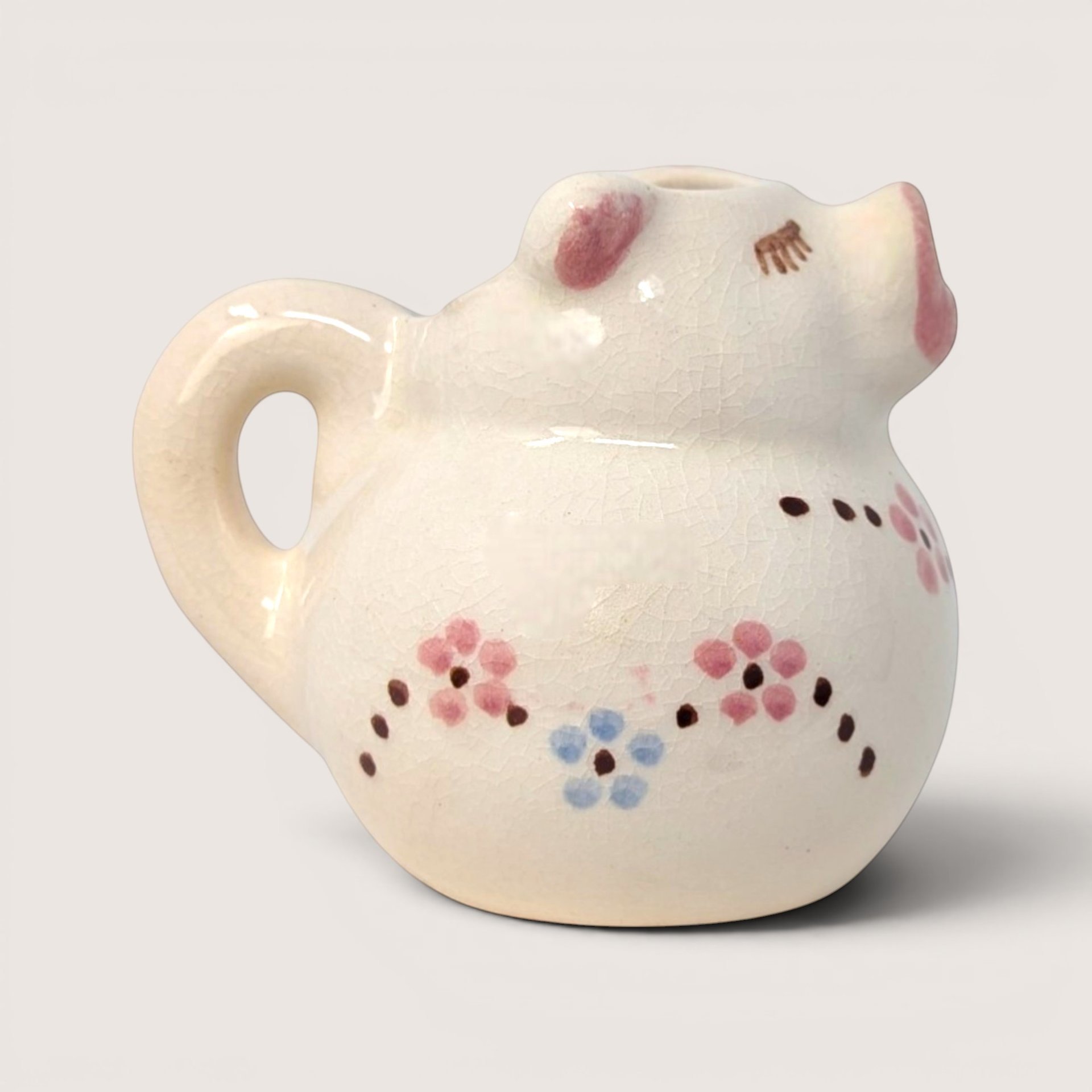 Vintage hand-painted ceramic pig creamer pitcher with small pink and blue flowers and a glossy crazed finish.