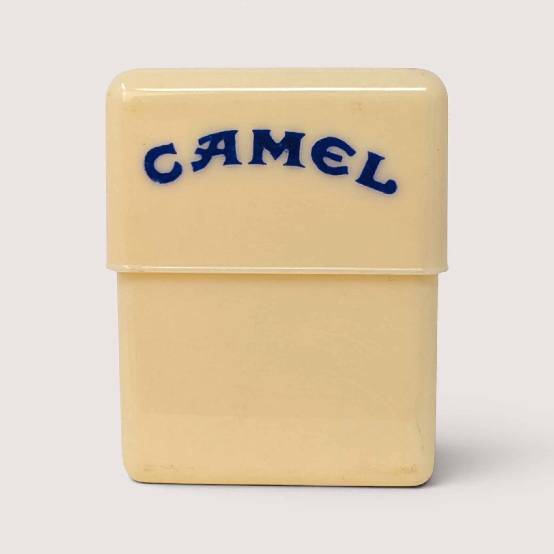 Vintage cream-colored plastic Camel cigarette case featuring the brand name in blue text on the lid.