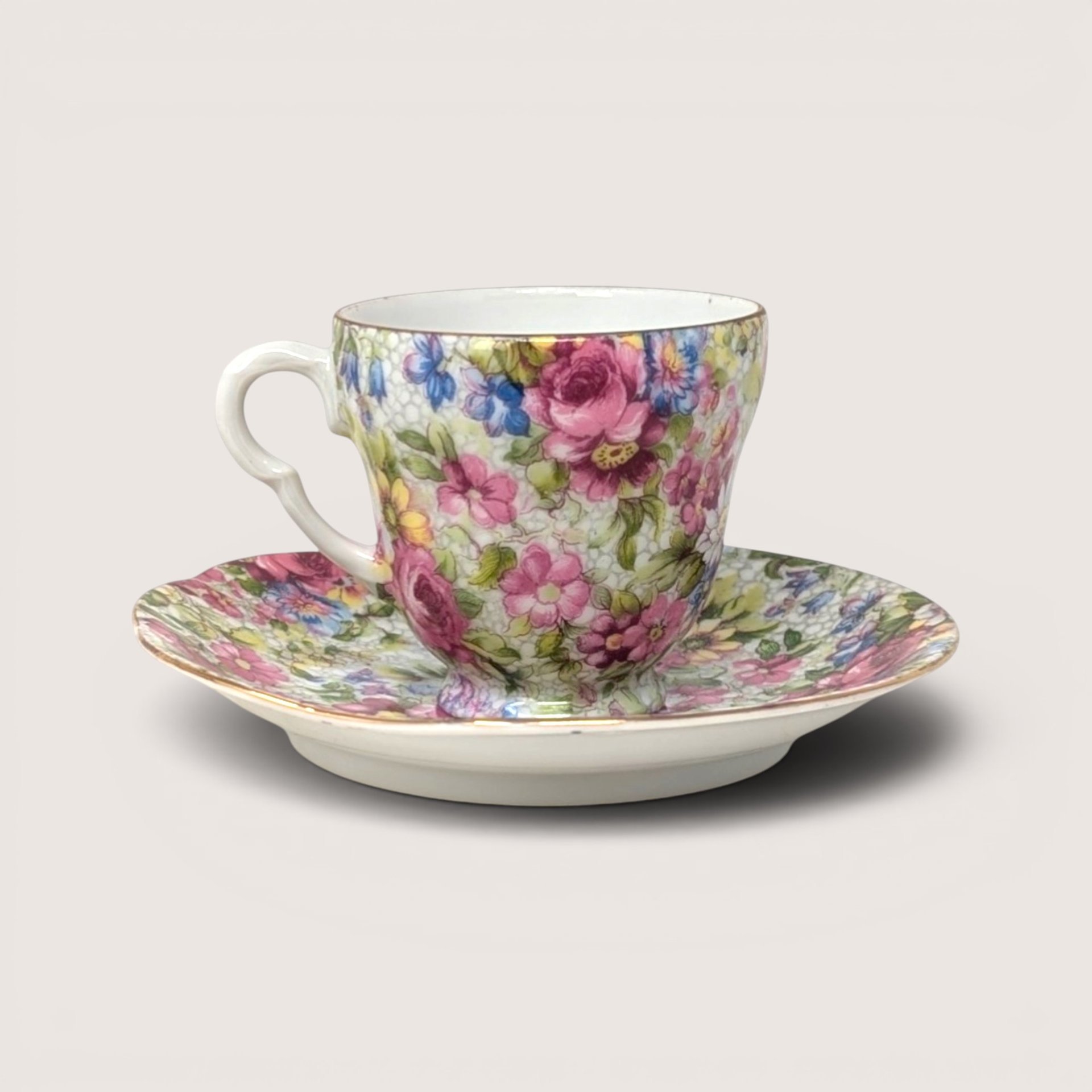 Vintage Trimont Occupied Japan demitasse cup and saucer decorated in a dense pink and blue chintz floral pattern.