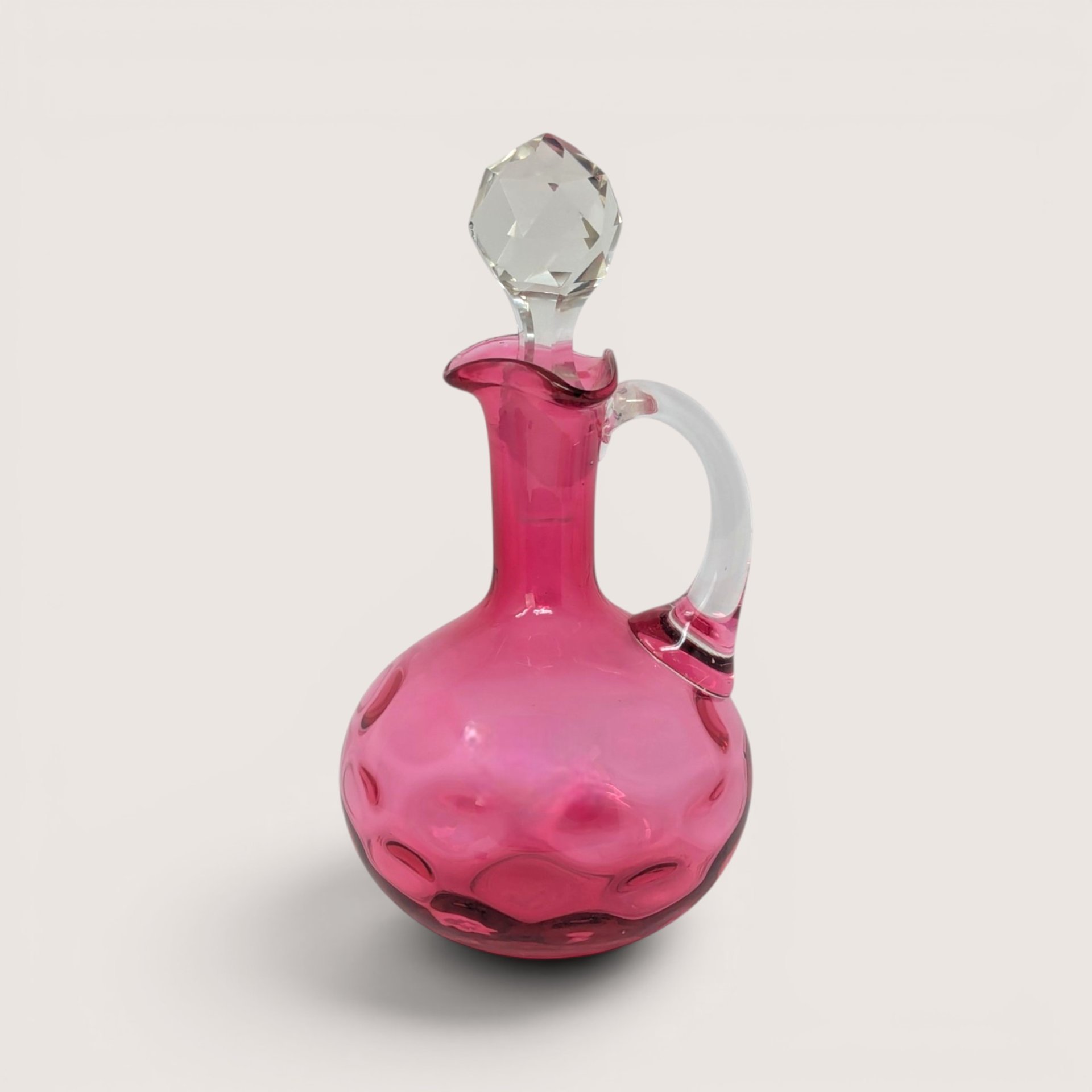 A vintage Fenton cranberry glass coin dot cruet with a clear applied handle and a faceted crystal stopper.