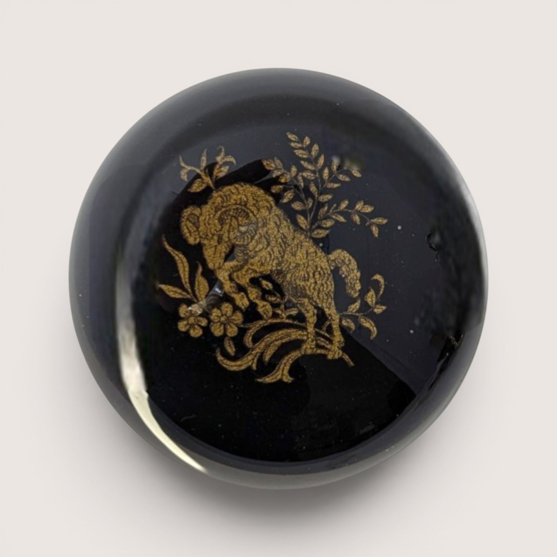 Vintage dome glass paperweight featuring an etched gold ram motif over a jet black lacquer background.