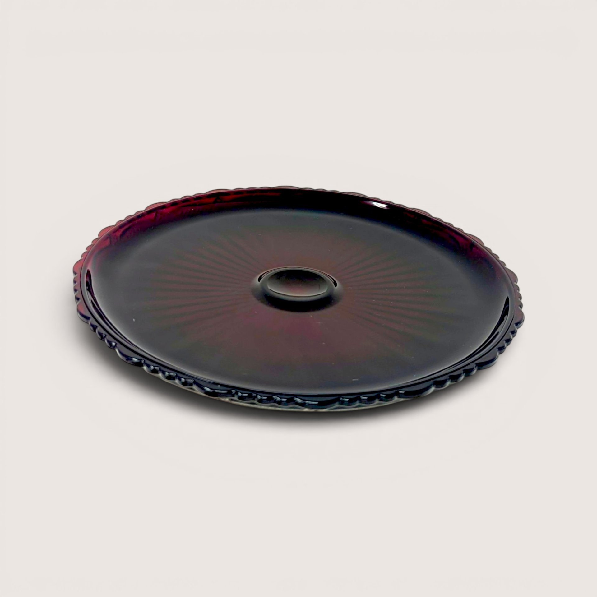 Vintage 1970s Avon Cape Cod ruby red pressed glass pie plate showing a detailed geometric rosette pattern from above.