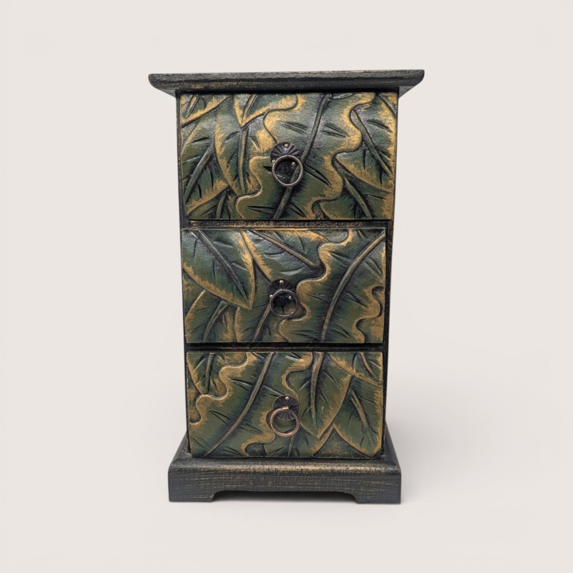 Vertical wooden mini chest with three carved leaf pattern drawers painted in antiqued green and gold with brass ring pulls.