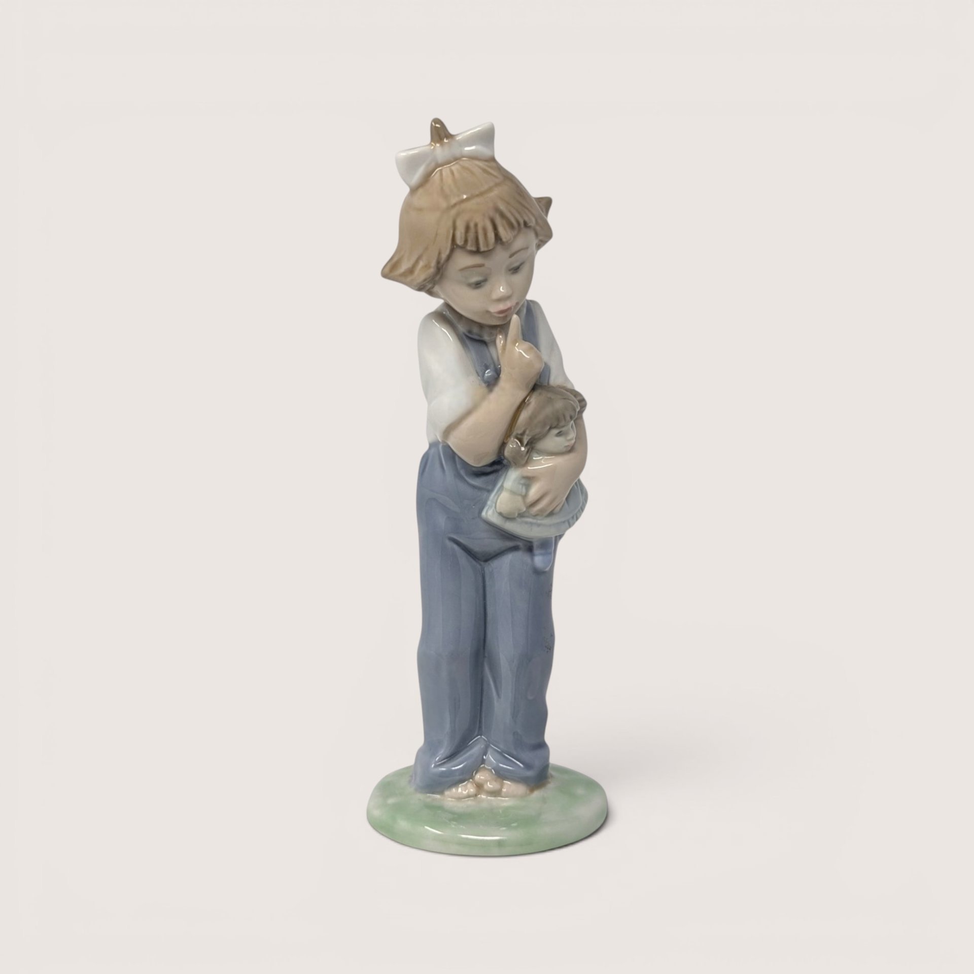 Vintage Nao by Lladro glossy porcelain figurine of a young girl in blue overalls hushing the doll in her arms.