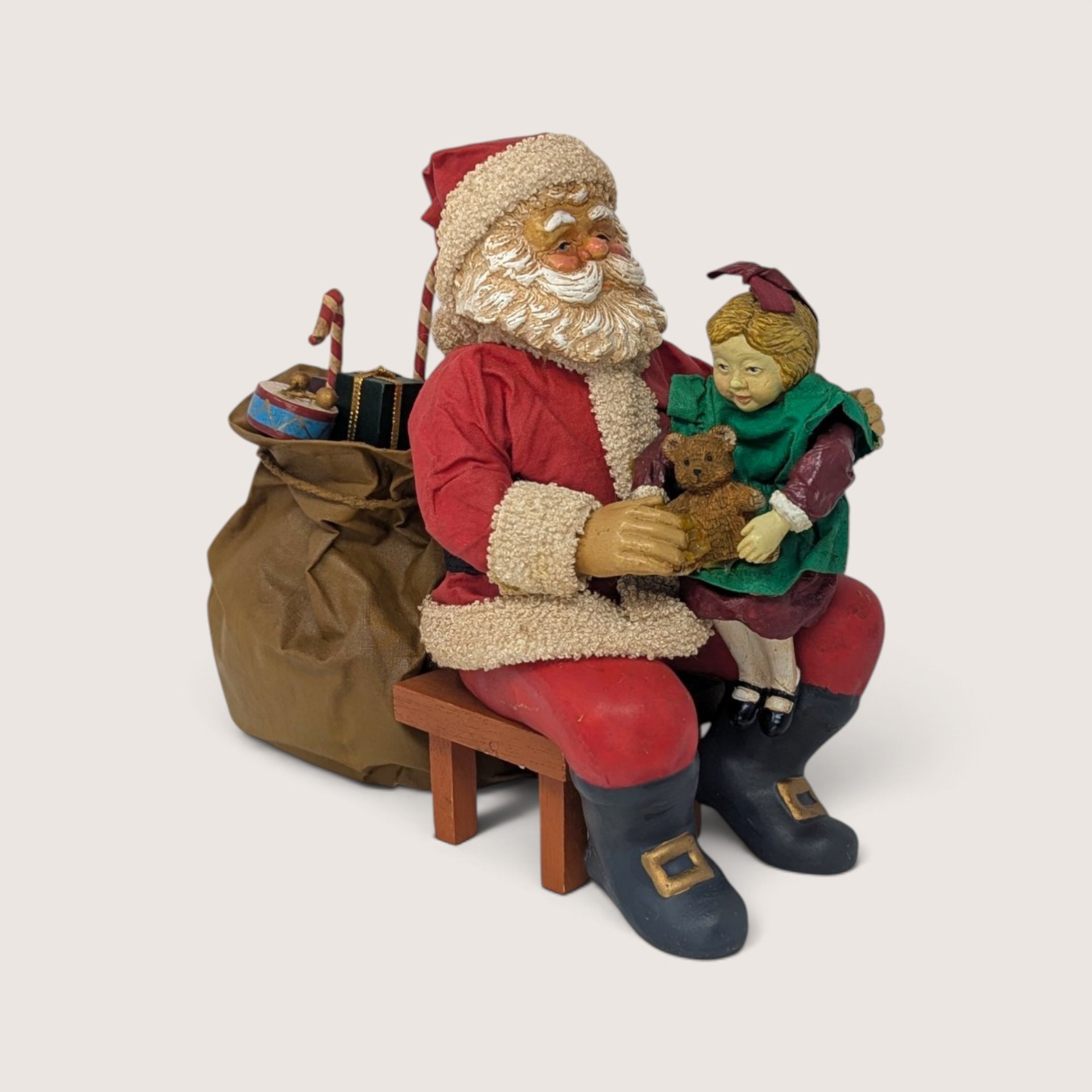 Vintage holiday figurine of Santa Claus sitting on a wooden bench holding a young girl on his lap.