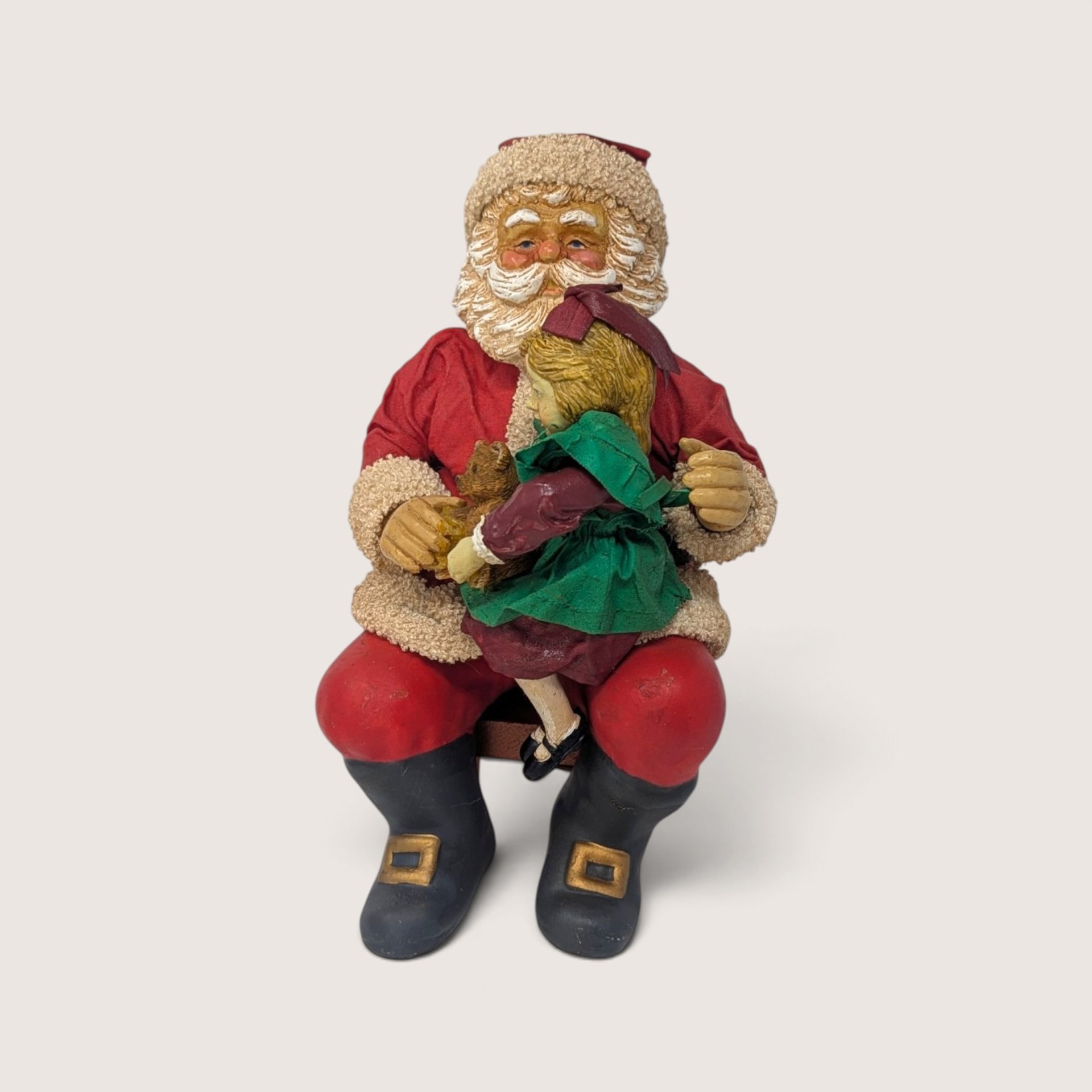 Vintage holiday figurine of Santa Claus sitting on a wooden bench holding a young girl on his lap.