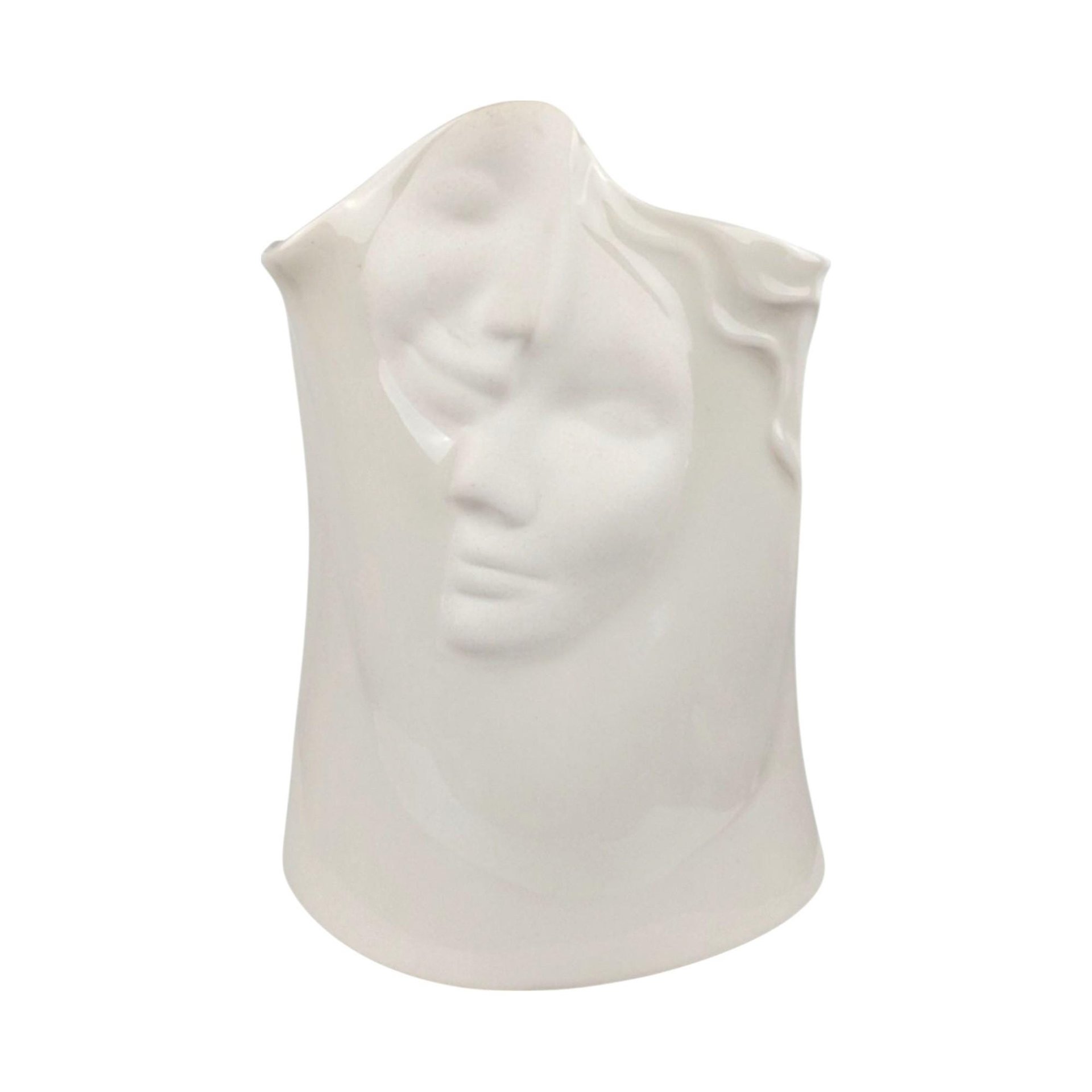 A minimalist, all-white porcelain vase sculpted in the shape of a serene female face. The vase features an elongated neck and a stylized head, with flowing hair textured into the ceramic. The entire piece is finished in a clean, high-gloss white glaze, emphasizing the smooth contours and delicate facial features without the use of color.