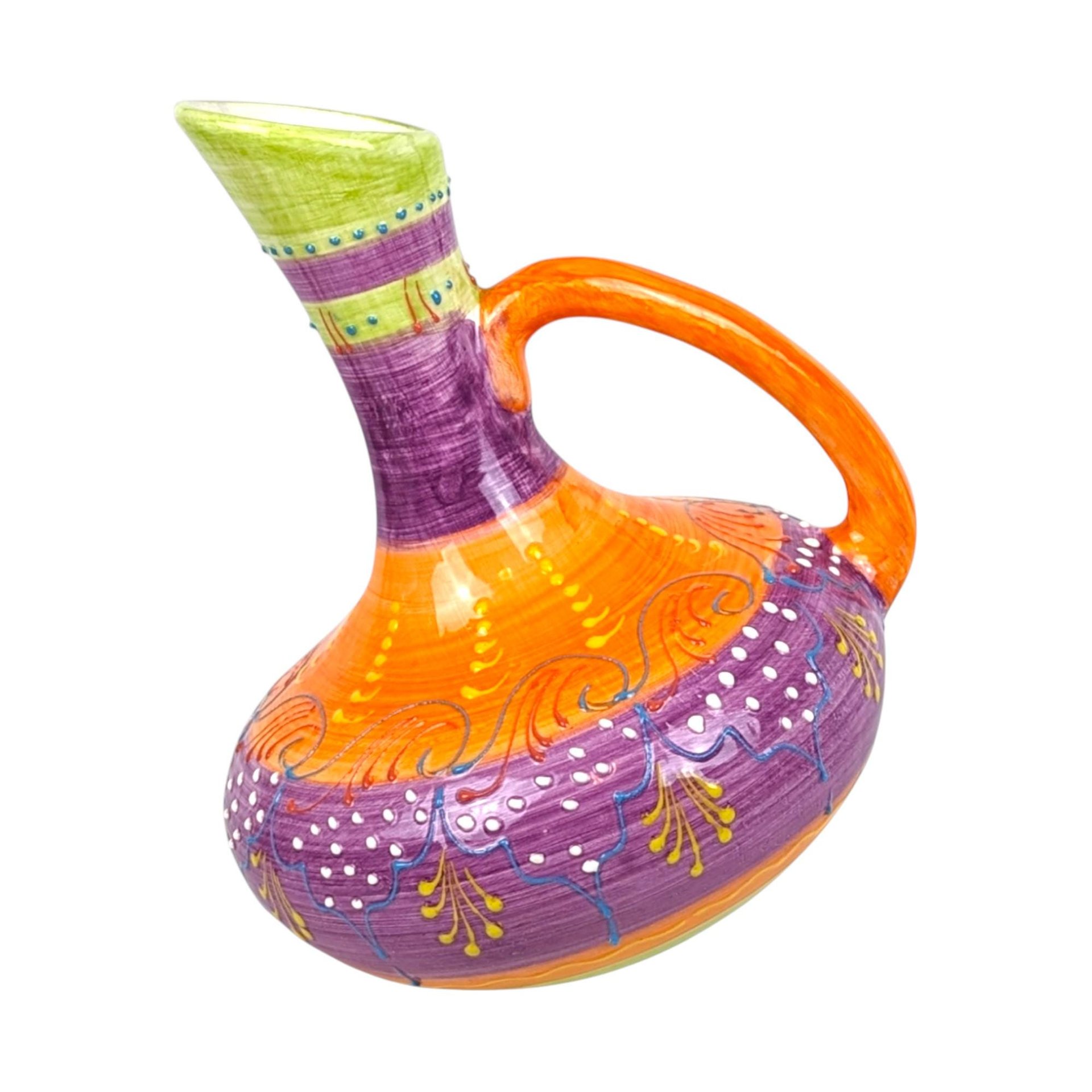 A 9-inch tall handmade ceramic pitcher with a unique slanted or tilted shape, featuring vibrant hand-painted stripes and dot patterns in purple, orange, green, and blue.