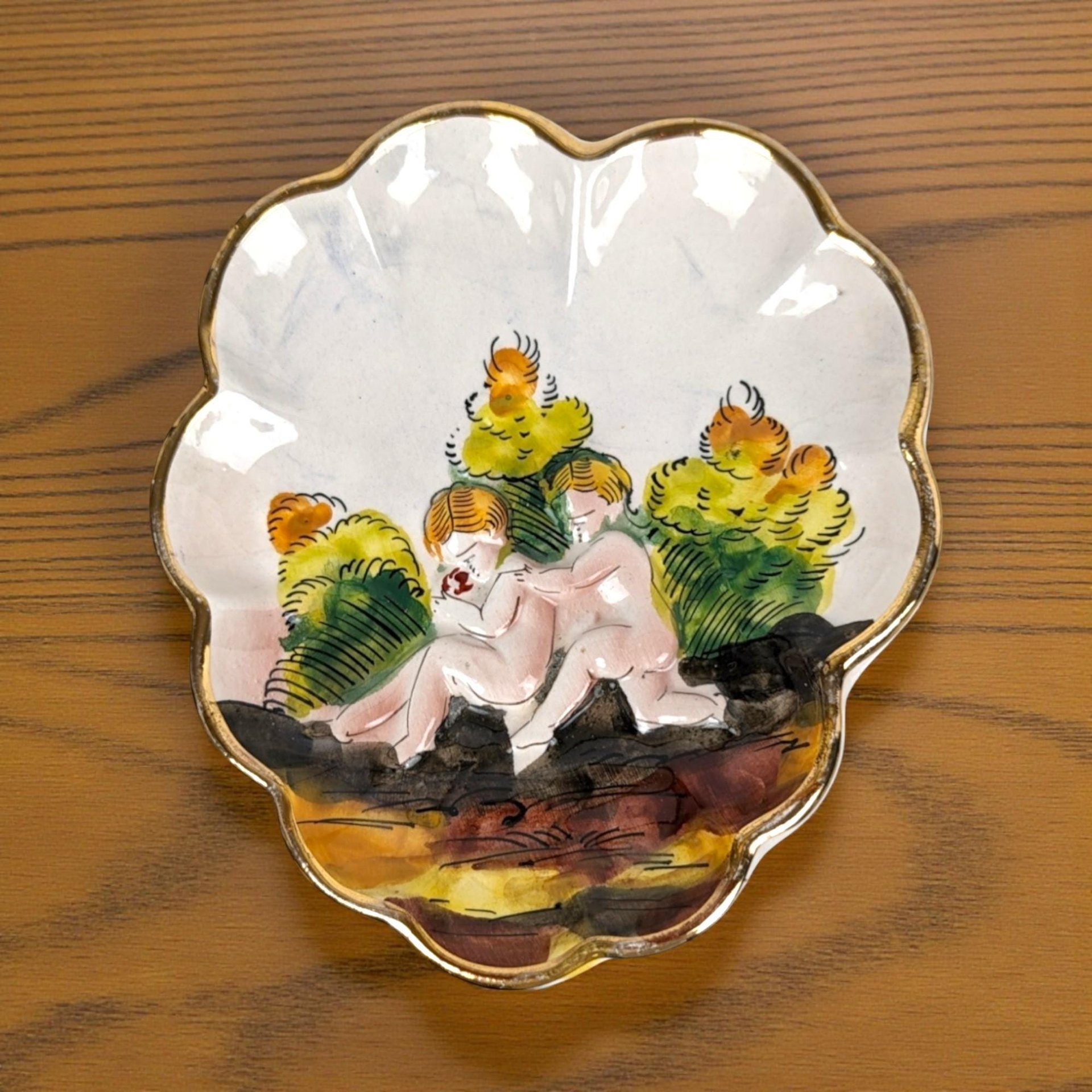 A white heart-shaped or oval ceramic trinket dish featuring hand-painted raised relief figures of children playing in a nature scene with a gold-gilded rim.