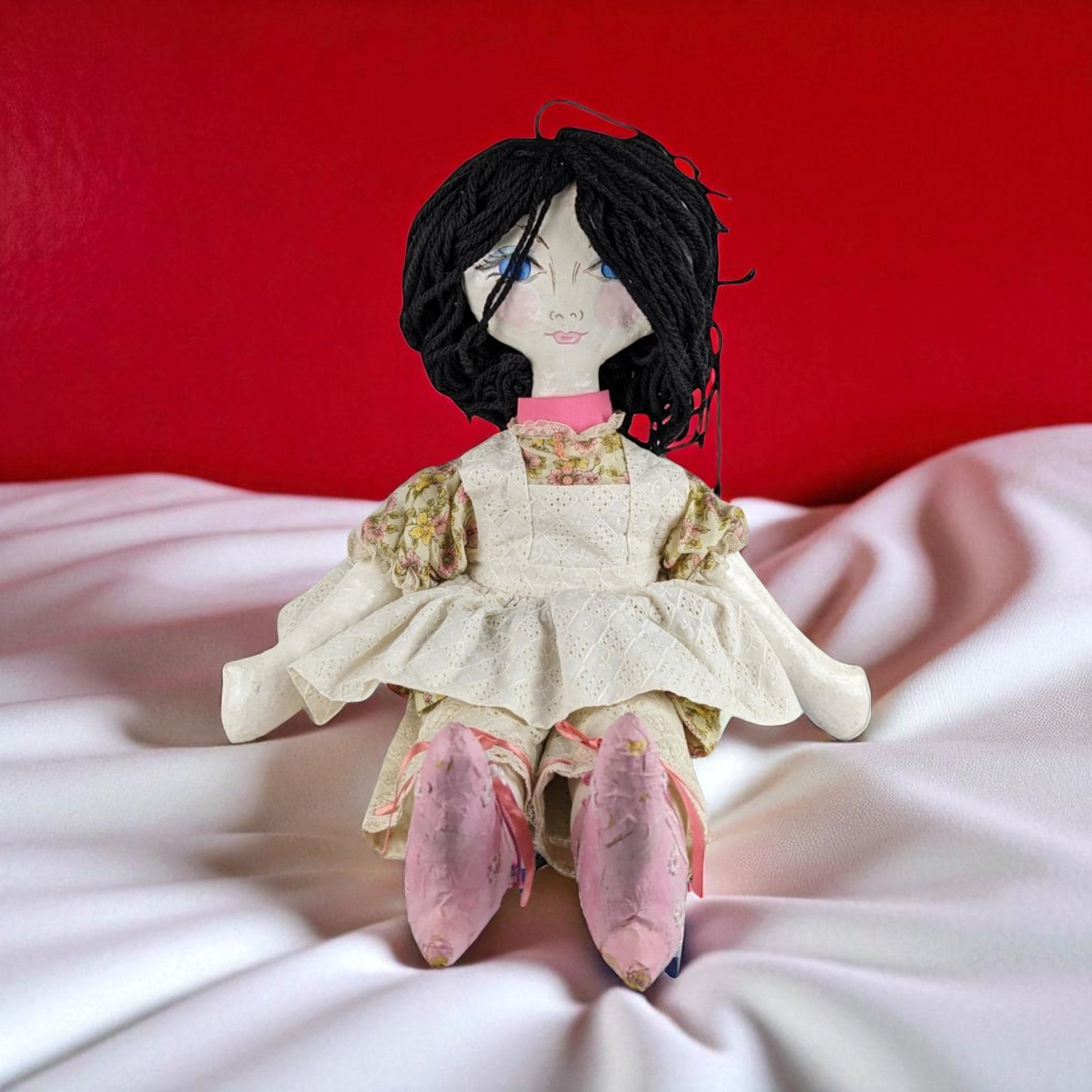 A large 25-inch handmade doll with a hand-painted paper mache head, hands, and feet, featuring black yarn hair, blue eyes, and wearing a floral dress with a white eyelet pinafore.