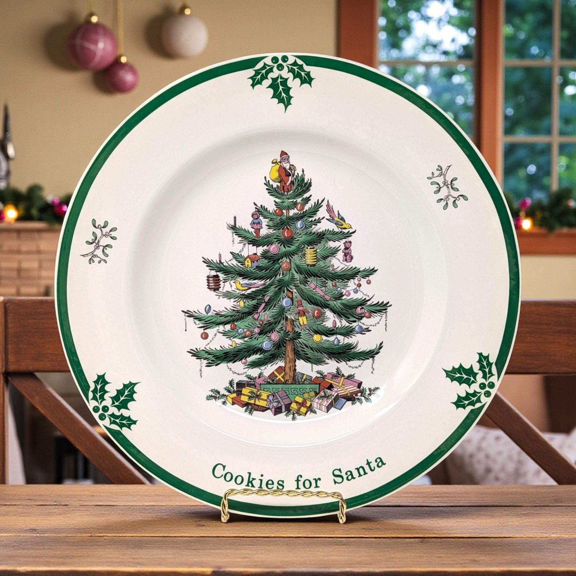 A large round porcelain plate featuring the iconic Spode Christmas tree at the center, decorated with colorful ornaments and topped with a tiny Santa. Bold, festive lettering reads 'Cookies for Santa' around the rim, accented with holly sprigs and a crisp green border.