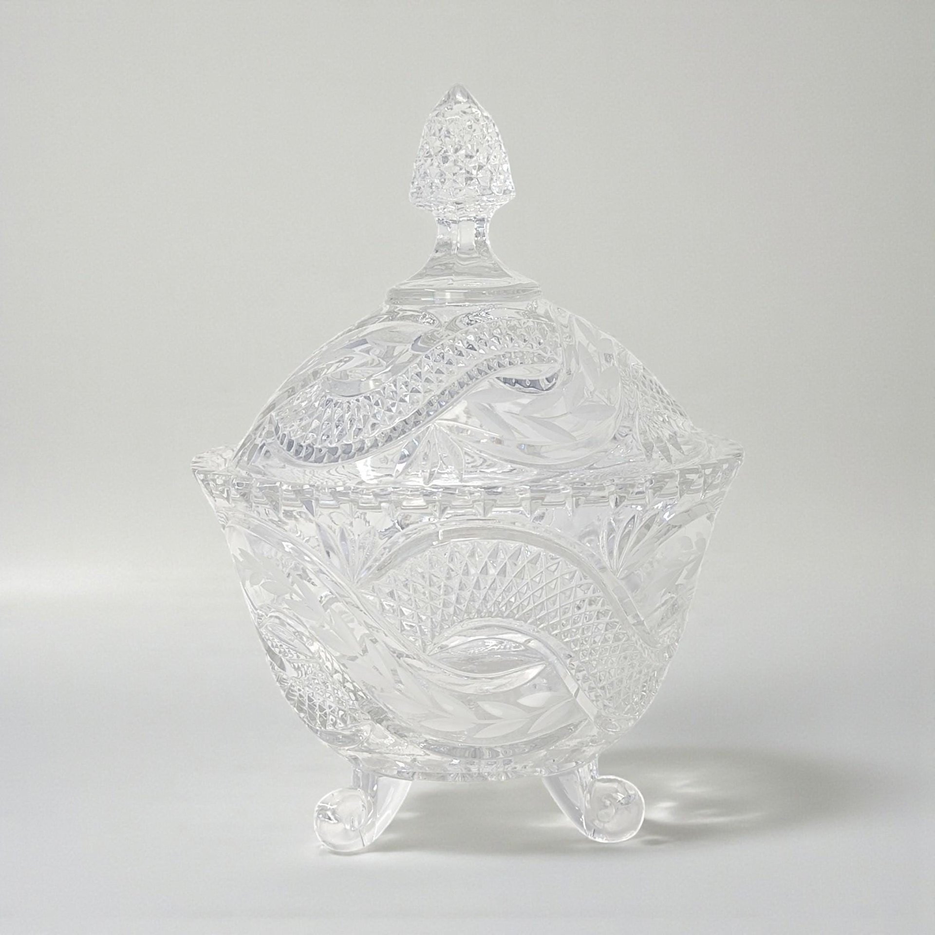 A tall, clear crystal candy dish with a matching lid. The exterior features a bold, swirling serpentine texture that winds around the body and finial, creating a fluid, rippled glass effect.