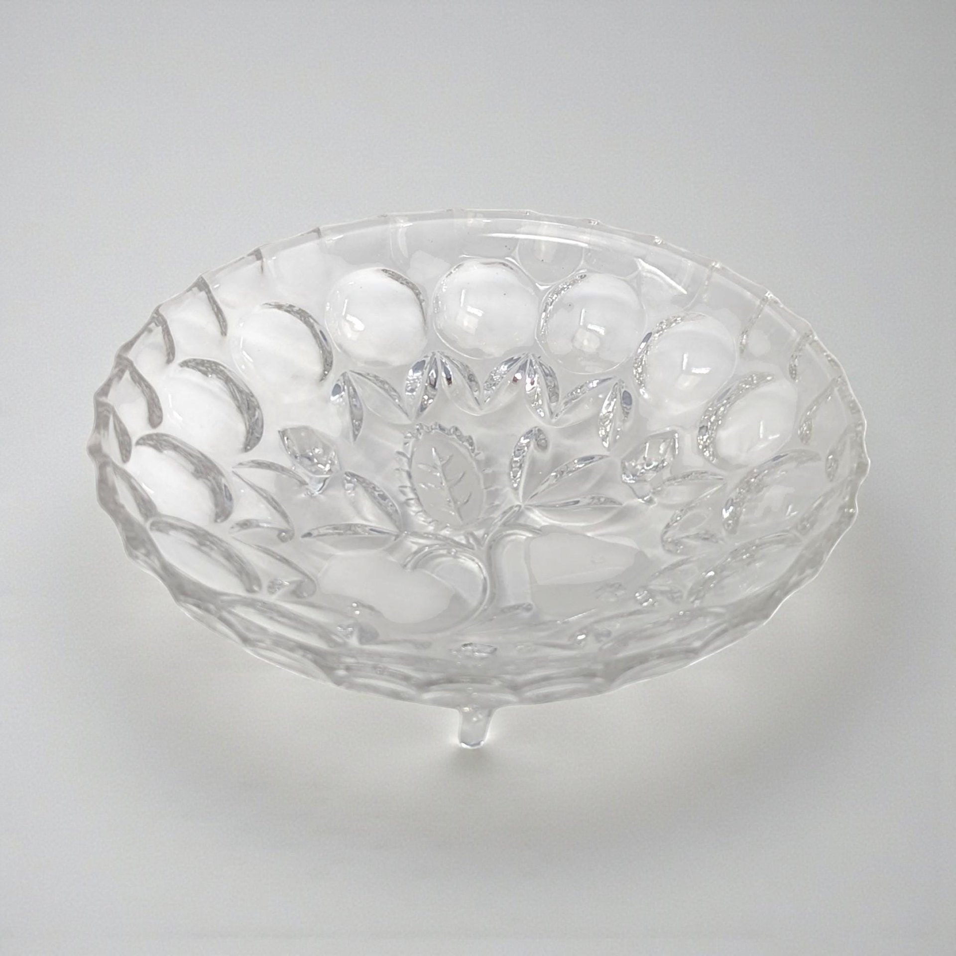 A clear pressed glass bowl with a subtle pedestal base. The interior features an intaglio fruit motif, while the rim is finished with a classic ruffled or "sawtooth" edge.