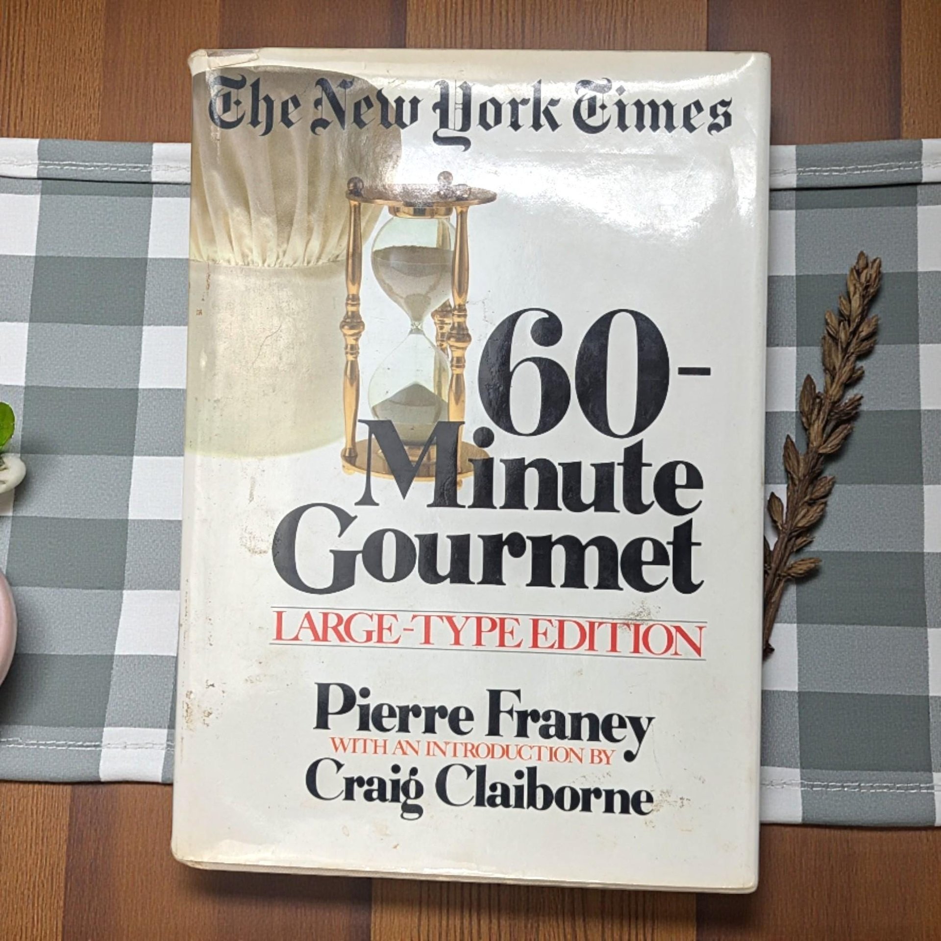 A large hardcover cookbook with a white dust jacket featuring a colorful illustration of a chef's hat, vegetables, and a whisk.