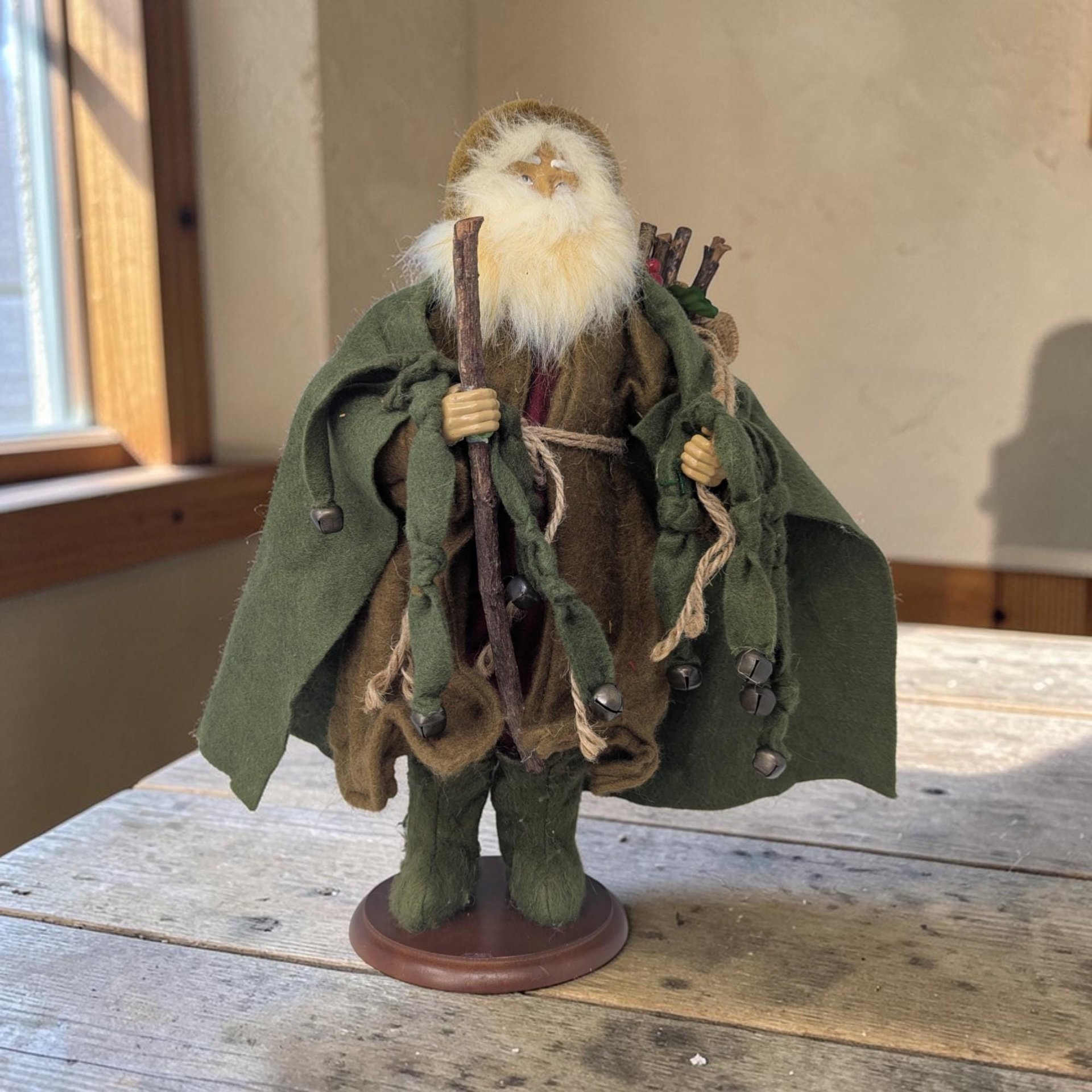 A tall Santa figure wearing a brown and green forest-themed outfit. The texture is a mix of soft faux fur, smooth cloth, and a matte plastic face in a tall, upright silhouette with a circular base.