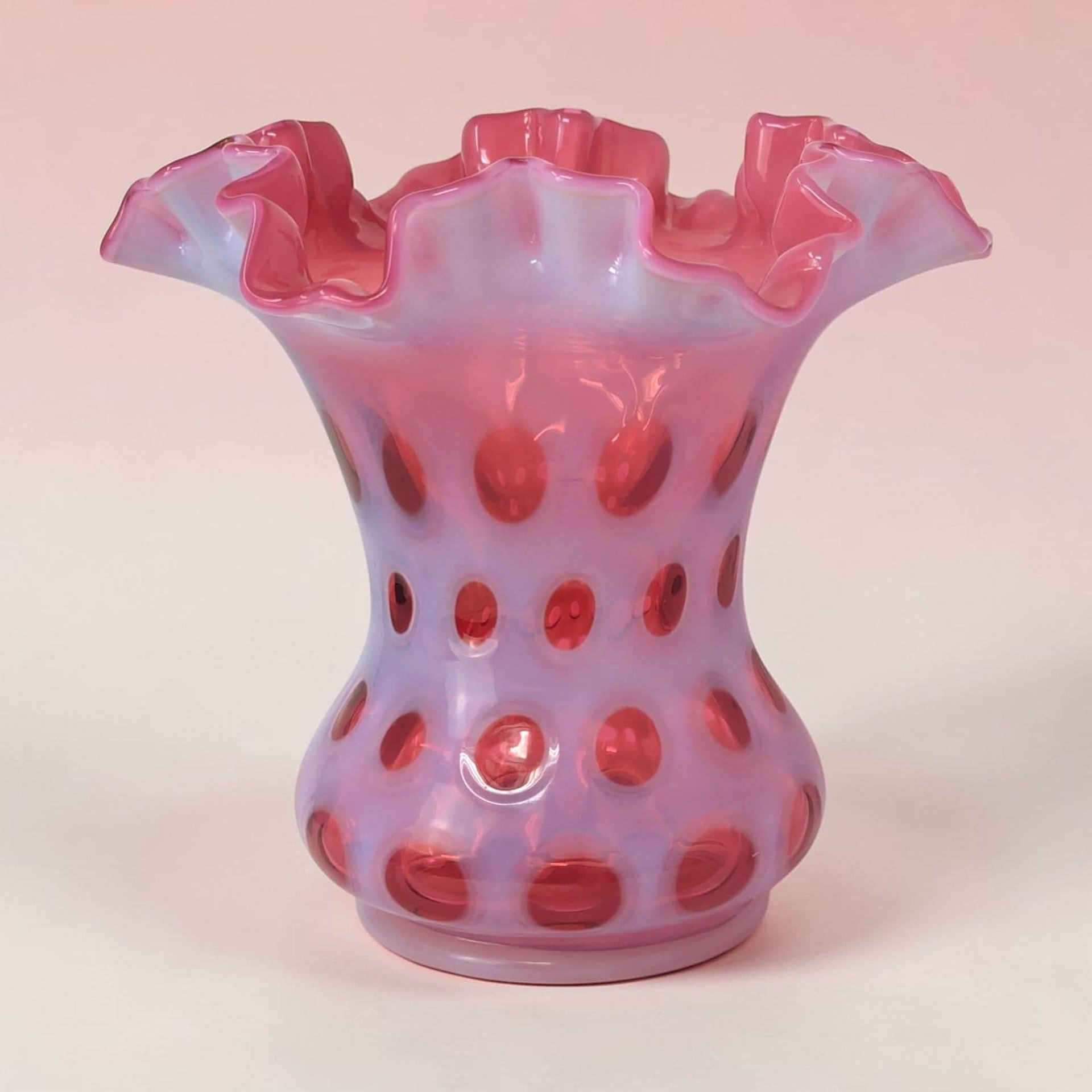A bulbous cranberry glass vase featuring an opalescent coin dot pattern and a dramatic, wide ruffled rim.