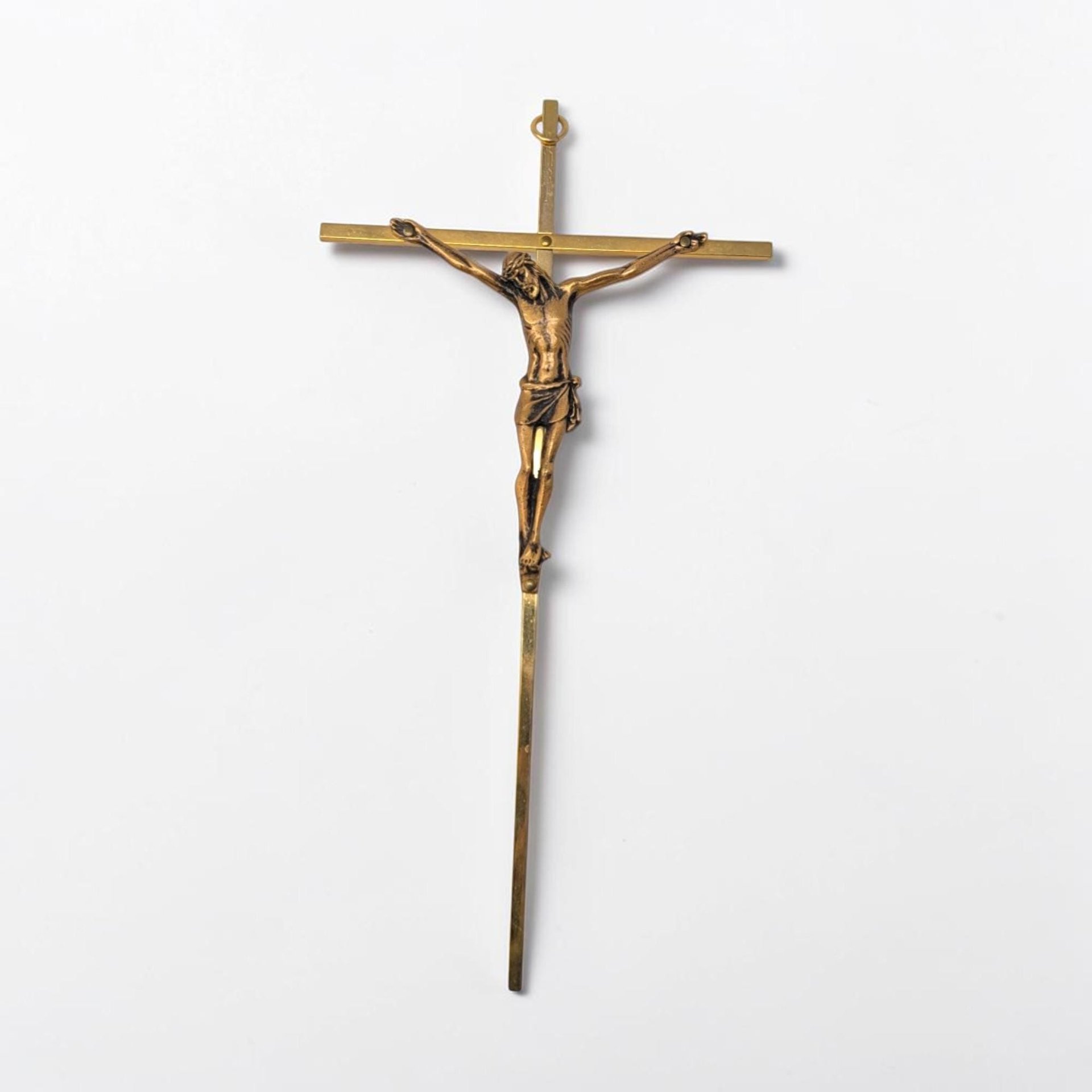 A slender, polished gold-tone metal crucifix with an ornate flared cross design. The figure of Christ is rendered in high relief with a small INRI plaque positioned at the very top of the vertical beam.
