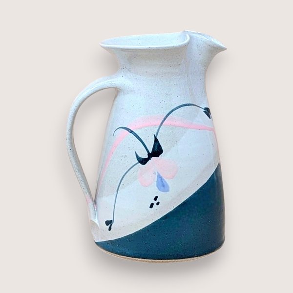 Speckled cream earthenware pitcher with a wide flared rim and sturdy handle. Features a hand-painted abstract floral design in teal, pink, and indigo with a diagonal teal color-block base.