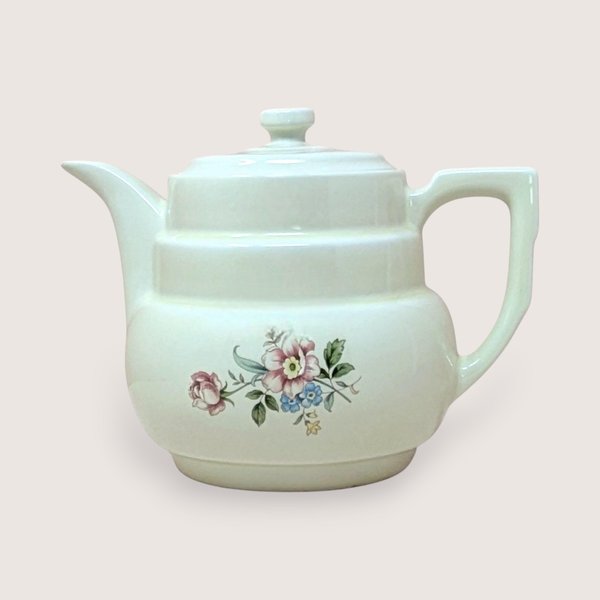 Hall China "Rambling Rose" cream ceramic coffee pot and lid. Features a tiered Art Deco body, an angular handle, and a delicate pink and blue floral spray. 7.75 inches tall.