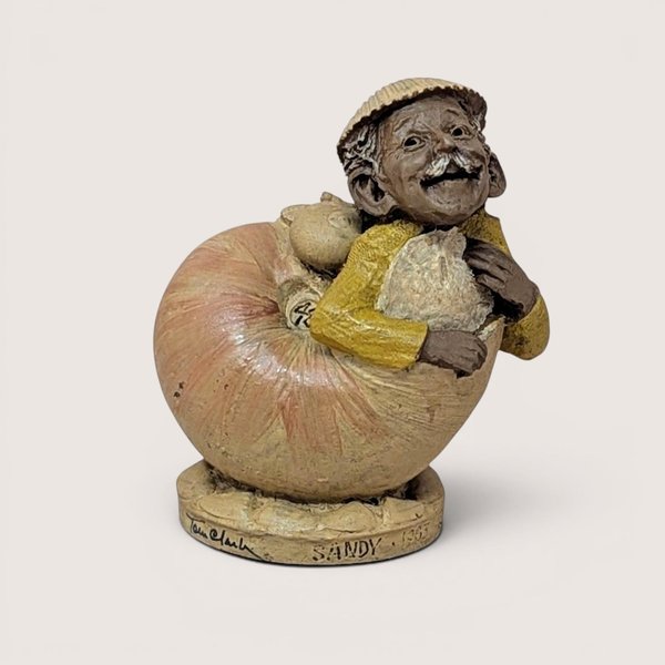 Tom Clark "Sandy" gnome figurine peeking out of a shell, isolated on a light neutral background.