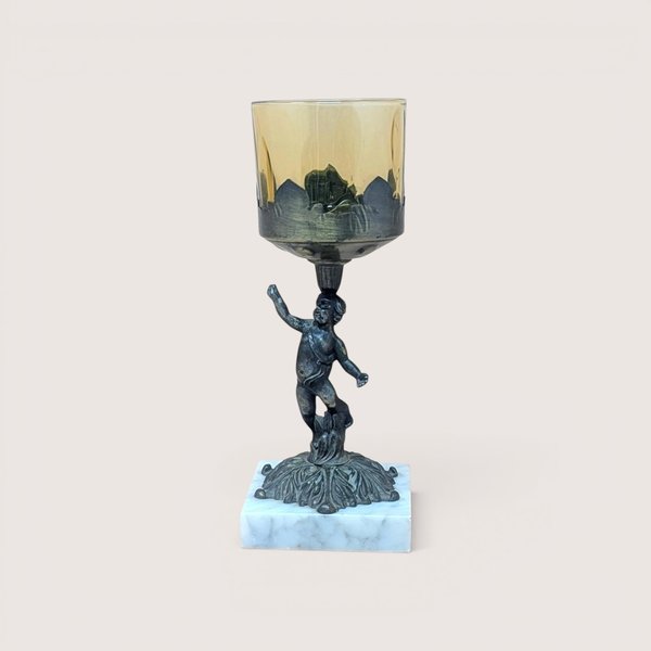 A 9-inch vintage candle holder featuring a dark cast metal cherub figure standing on a white marble square base, supporting a translucent amber glass cup.
