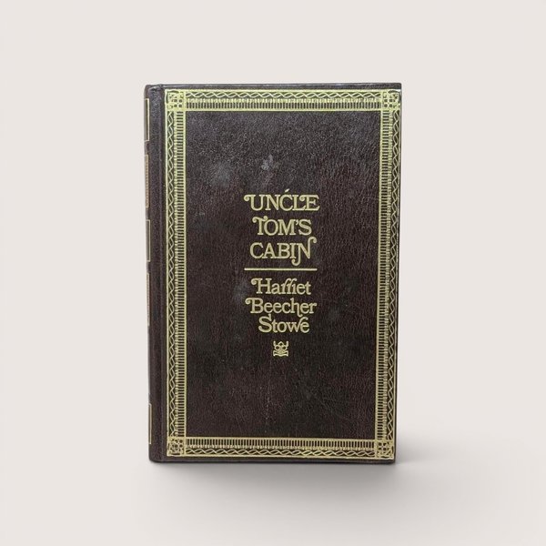 A 1976 hardcover edition of Uncle Tom's Cabin by Harriet Beecher Stowe with a dark brown textured cover and gold gilt lettering and borders