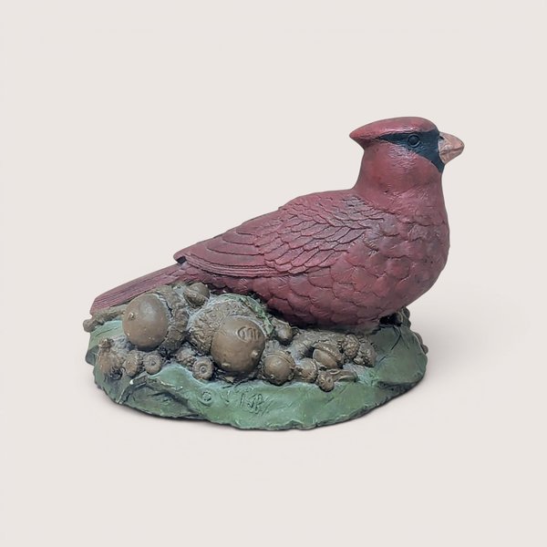 A hand-painted resin sculpture of a red cardinal perched on a bed of acorns and green leaves against a neutral background.