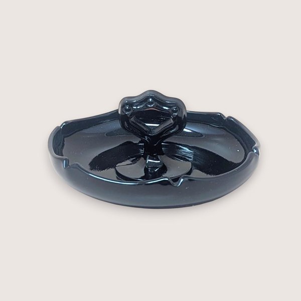 Glossy black amethyst glass trinket dish with a scalloped perimeter and a unique, ornate center handle featuring circular cutouts. The deep violet undertones are visible only under intense light.