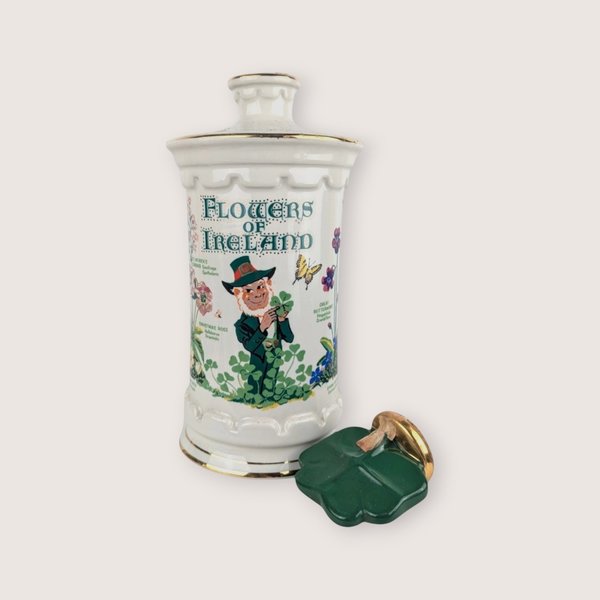 White ceramic empty liquor decanter with a Flowers of Ireland leprechaun design and a broken green shamrock stopper.