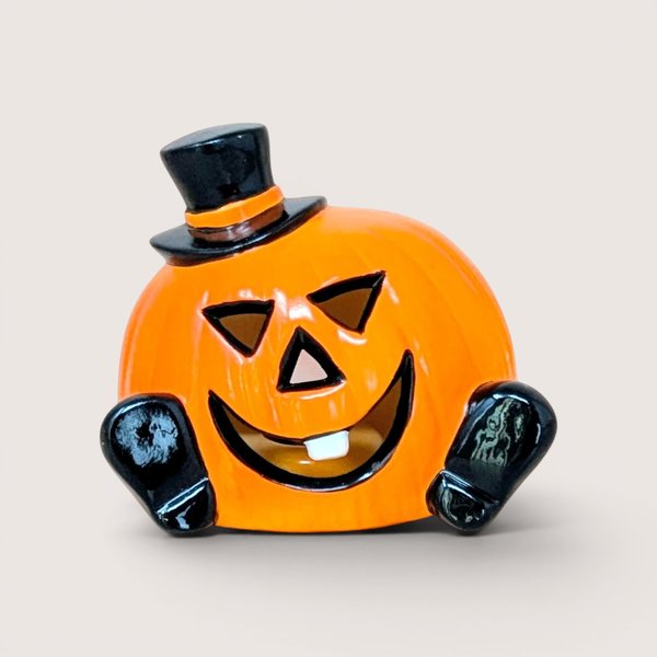 A glossy orange ceramic pumpkin figurine wearing a black top hat and featuring a single white tooth against a neutral background.