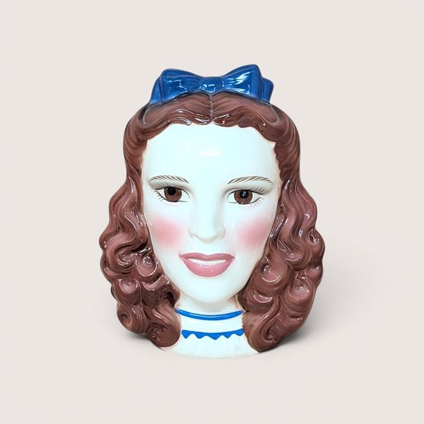 A vintage hand-painted ceramic wall mask of Dorothy from The Wizard of Oz, featuring her iconic pigtails and a bright blue hair bow.