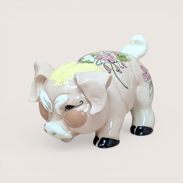 A vintage Kay Finch California pottery pig figurine with a pink floral pattern on its back and a humorous grumpy facial expression.