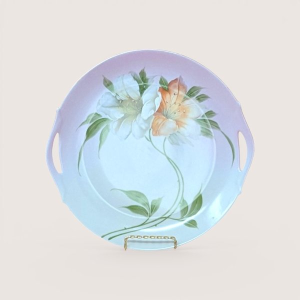A round porcelain handled plate with painted pink and white floral details, centered on a beige background.