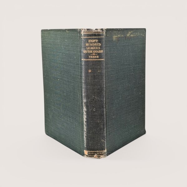 An antique green cloth book spine titled "Eight Hundred Leagues on the Amazon" by Verne, centered on a beige background.