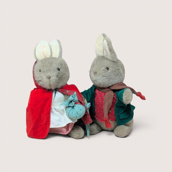 Two plush rabbit dolls dressed in vintage cloaks and winter clothing, centered on a beige background.
