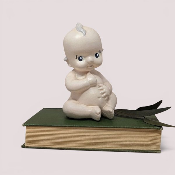 Vintage matte ceramic Kewpie baby doll talcum powder shaker seated with side-glancing eyes and a small chip on its ear.