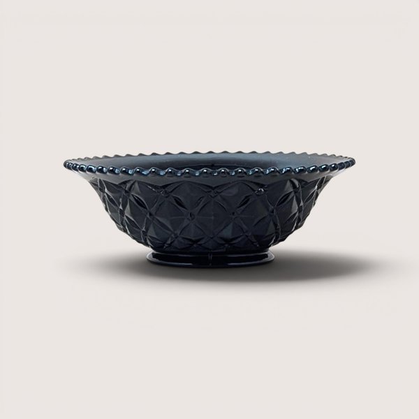 A vintage black glass bowl with a diamond pattern and beaded rim, centered on a beige background.