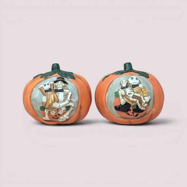 Set of two vintage 1990s ceramic pumpkin tealight holders with hand painted relief scenes of a skeleton couple.