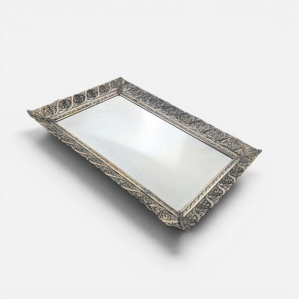 Vintage rectangular silver metal filigree vanity tray with a reflective mirrored surface on a white background.