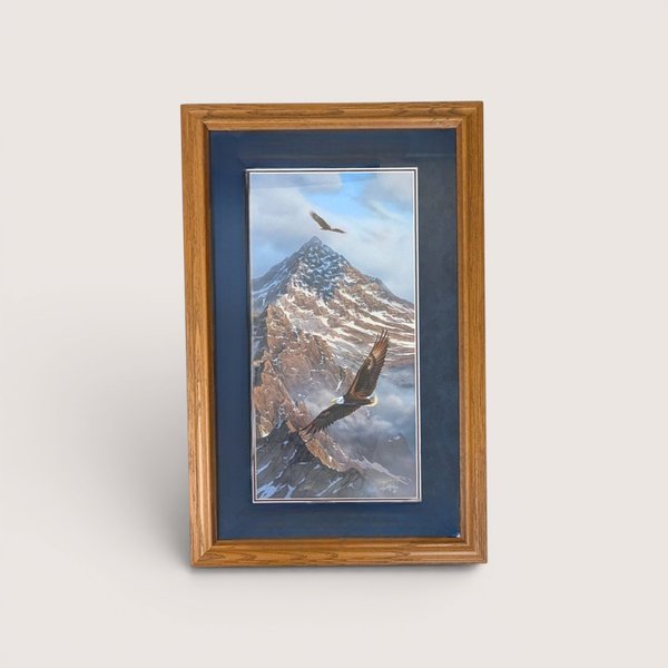 Framed wildlife print showing two bald eagles soaring over a snow covered mountain peak with a dark blue mat.
