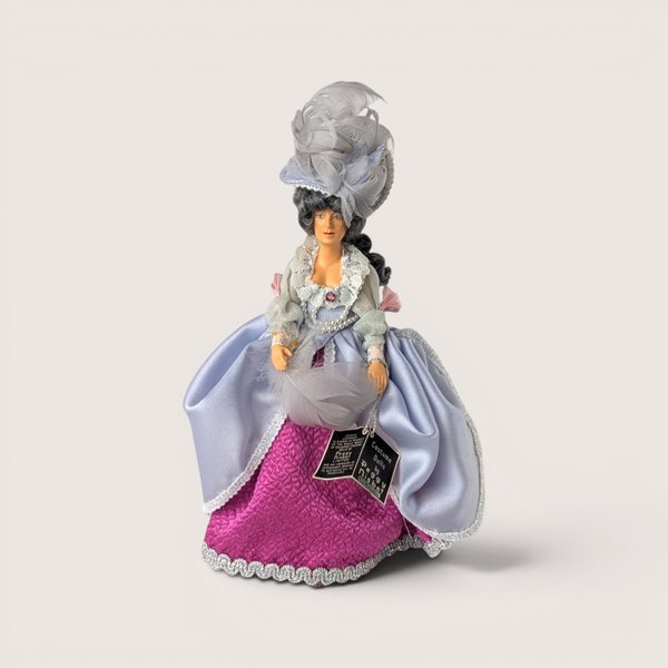 Vintage Peggy Nisbet Renoir portrait doll in an ornate lavender and pink gown with an elaborate feathered hat.